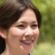 A woman smiling for the camera with trees in the background.